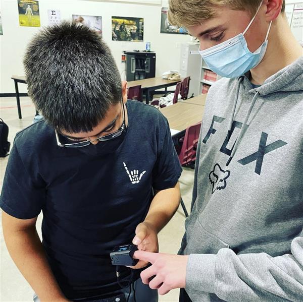 Two boys in health science, one is taking the other blood oxygen through a finger monitor.